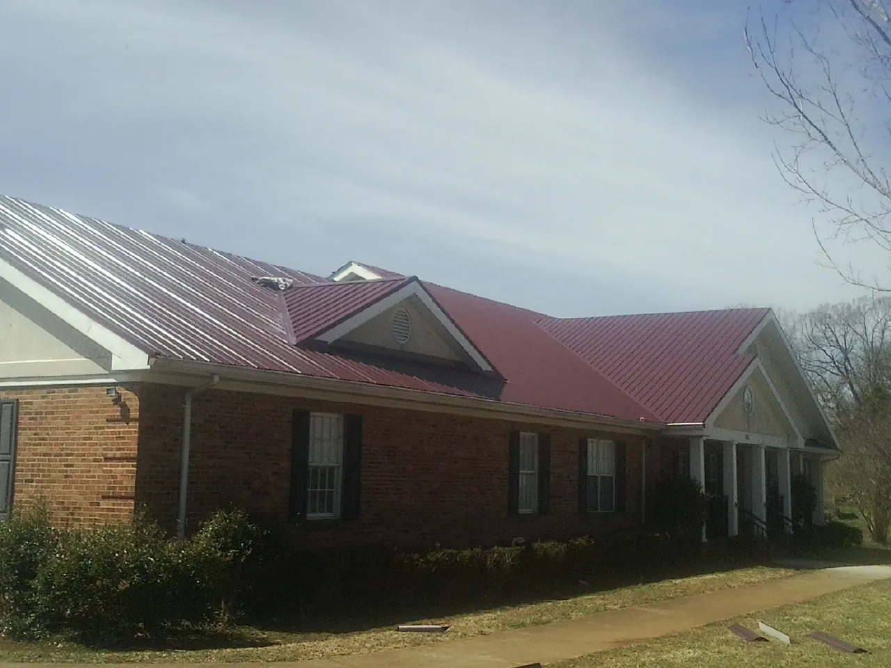 Red metal roof with gabled entries on a long brick building, from a Hail Damage Roof Repair job in Sudbury