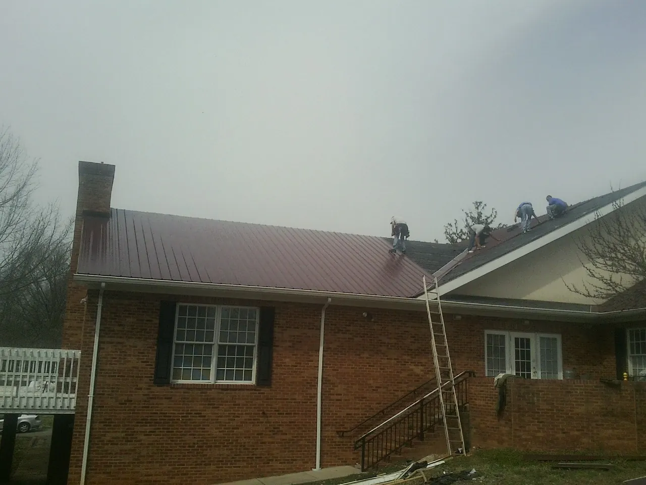Crew setting red metal roofing panels on a brick home in Sudbury