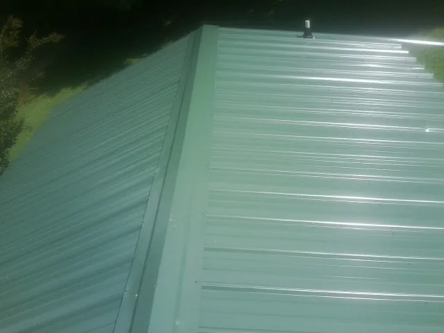 New green metal panels meeting at the ridge of a roof — Flat Roof Repair work by our crew in Sudbury