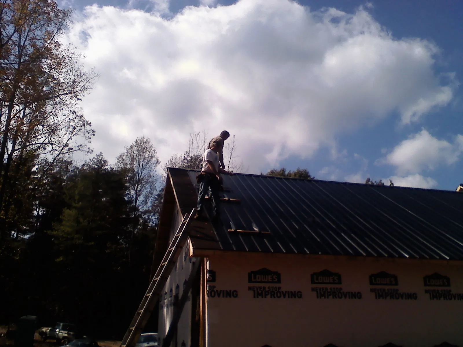 Roofer fastening dark metal panels high against a cloudy sky, from a Roof Inspection job in Sudbury