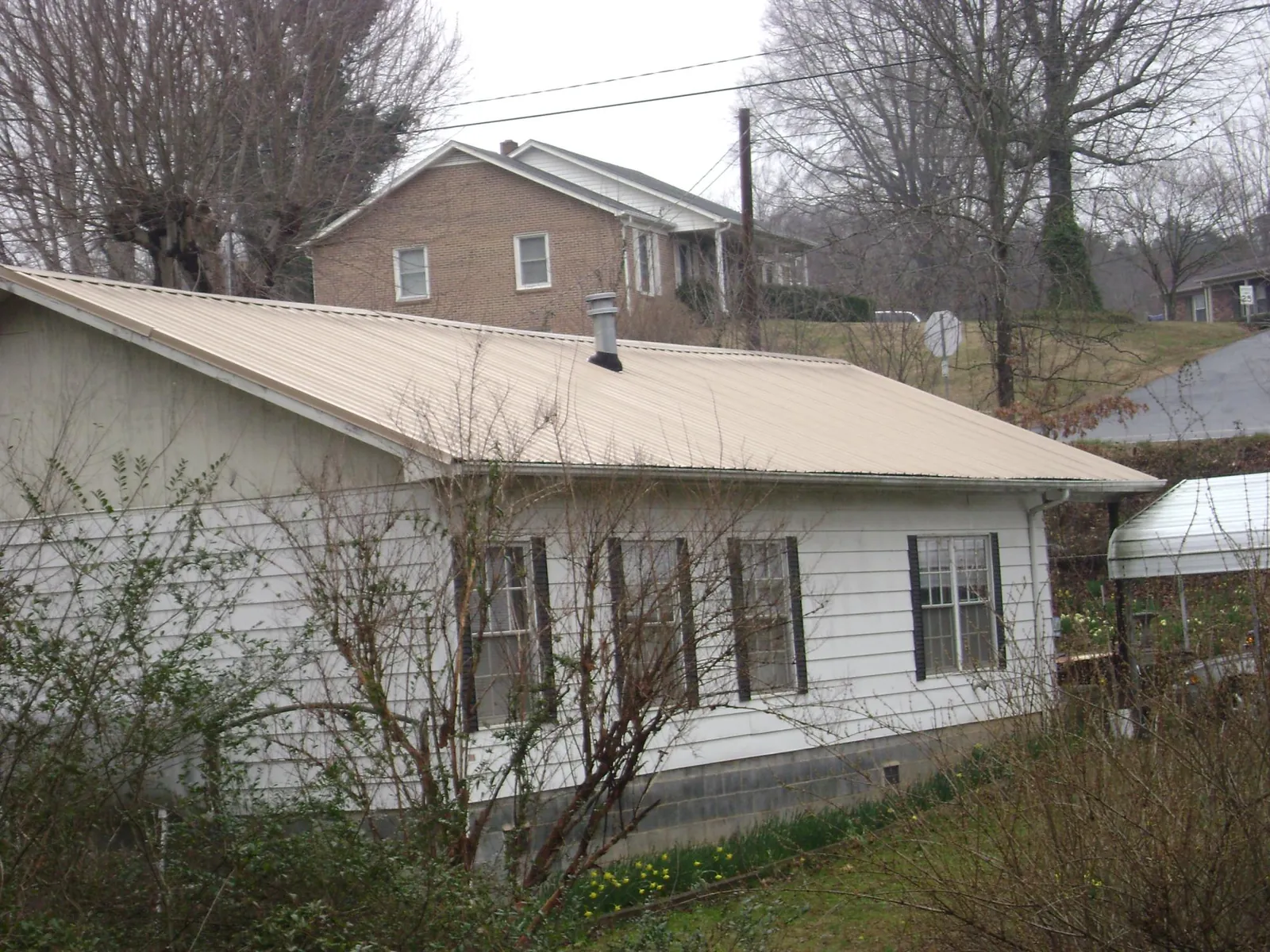 Tan metal roof on a white sided house set into a hillside — Commercial Roofing by Roofing Brothers in Sudbury