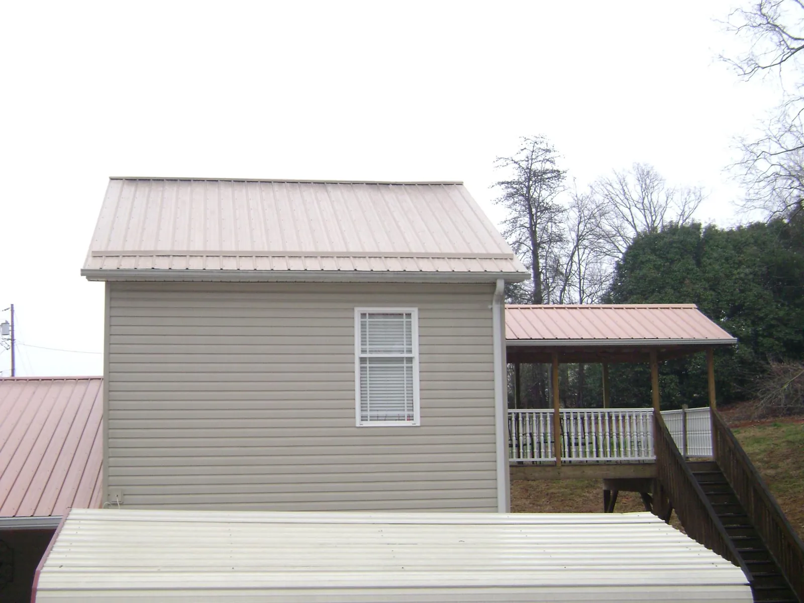 Tan metal roofs on a two story addition and attached porch, from a Roof Replacement job in Sudbury